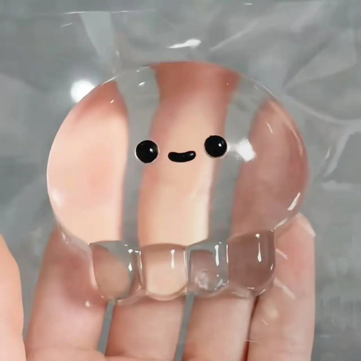 Translucent jellyfish squishy with a printed face draped over four fingers