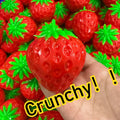 Strawberry Crunch Squishy held in a hand above a pile of red strawberries