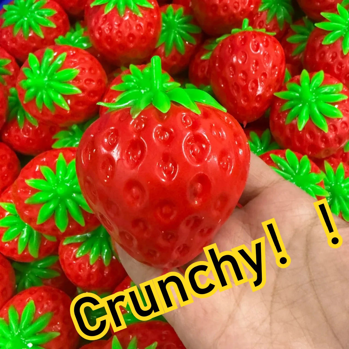 Strawberry Crunch Squishy held in a hand above a pile of red strawberries